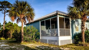 A small, single-story house with a porch, surrounded by palm trees and other vegetation. - The Rookery III Unit 4001 (Gulf Shores)