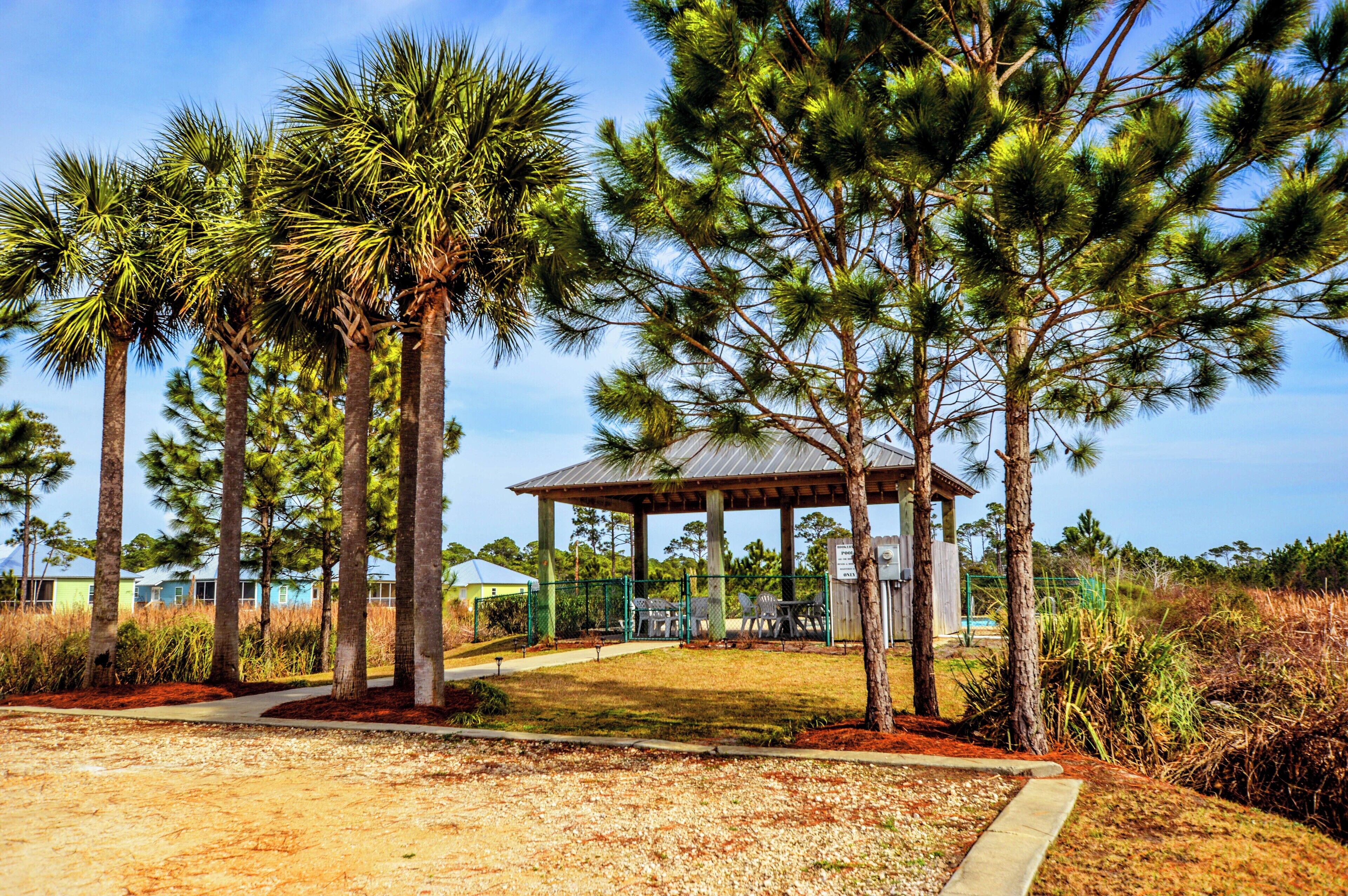 A gazebo with a roof and a bench area, surrounded by tall trees and a pathway.