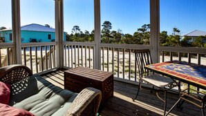 A covered outdoor area with a wooden deck, wicker furniture, and a table with a colorful tile top.