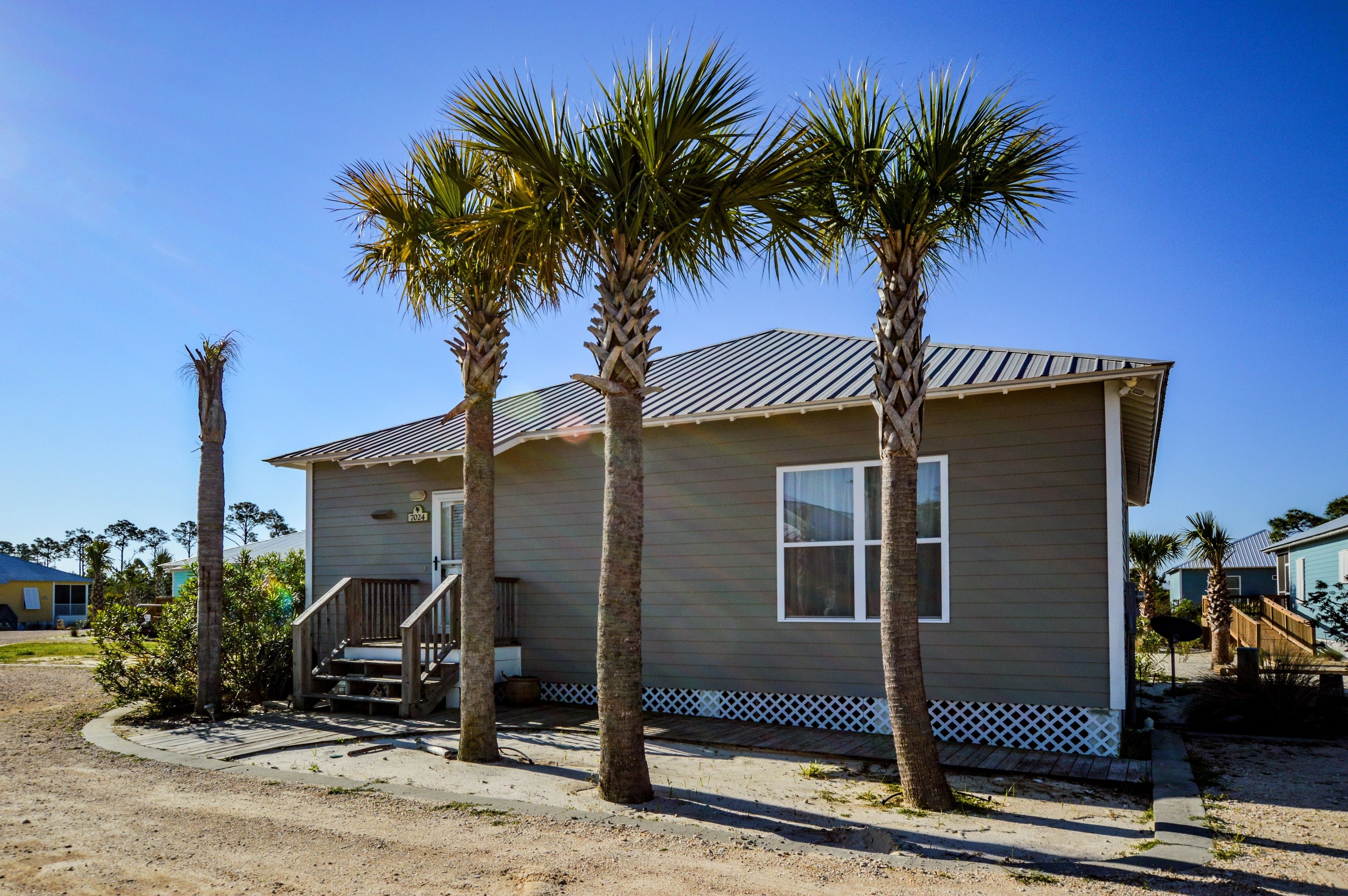 A single-story house with a front porch, palm trees, and a clear blue sky.