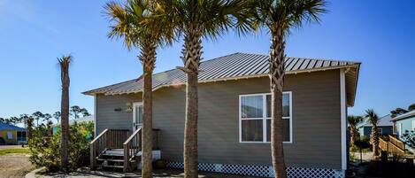 A single-story house with a front porch, palm trees, and a clear blue sky.