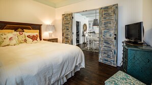 A bedroom with a large bed, a dresser, a television, and a door leading to a bathroom.
