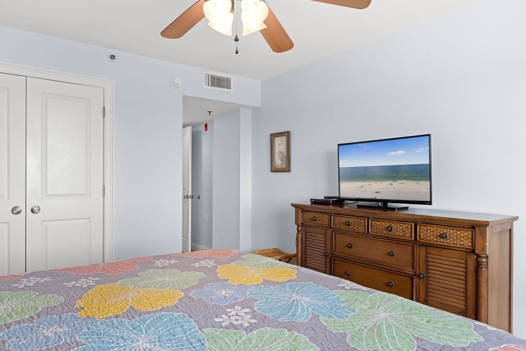 Une chambre à coucher avec un lit, un téléviseur posé sur une commode et un ventilateur de plafond.