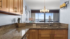 Eine moderne Küche mit Granit-Arbeitsplatten, Holzschränken, einer Edelstahl-Spüle und einer Kandelaberleuchte.