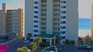 Ein mehrstöckiges Hotel namens Tropical Winds mit einem zentralen Eingang, Parkplatz und Blick auf den Ozean.