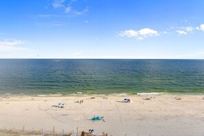 A beach with a wooden walkway leading to the water, sandy beach, and umbrellas. - Tropical Winds Unit 701 (Gulf Shores)