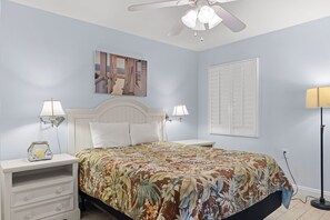 Une chambre à coucher comprenant un lit, des tables de chevet, un ventilateur de plafond et une lampe fixée au mur.