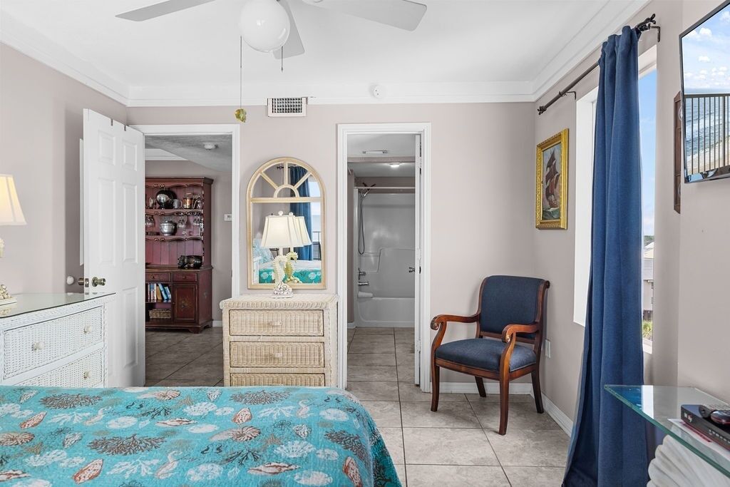 A bedroom with a bed, a chair, a dresser, a mirror, and a door leading to a bathroom.