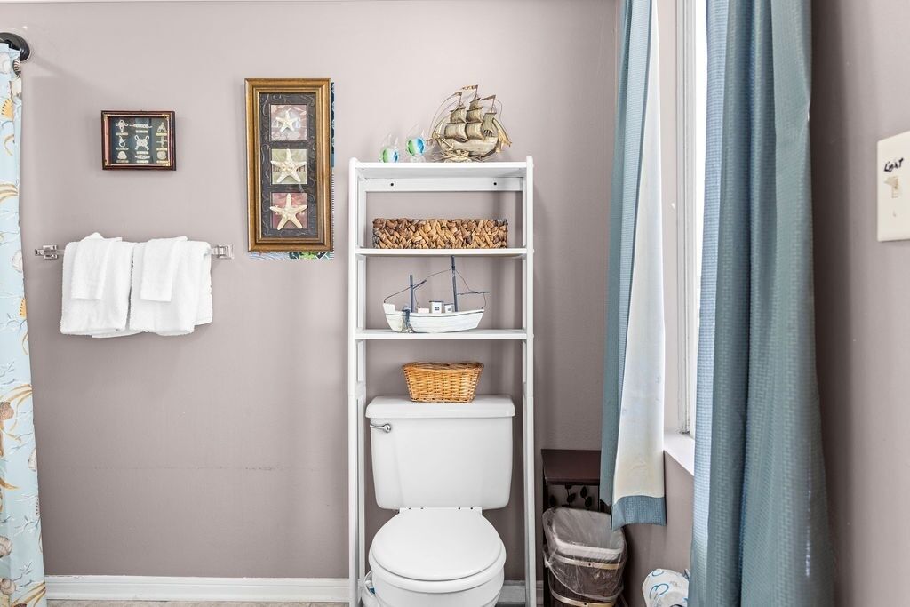 Een badkamer met een toilet, een plank met decoratieve objecten en een handdoekhouder.