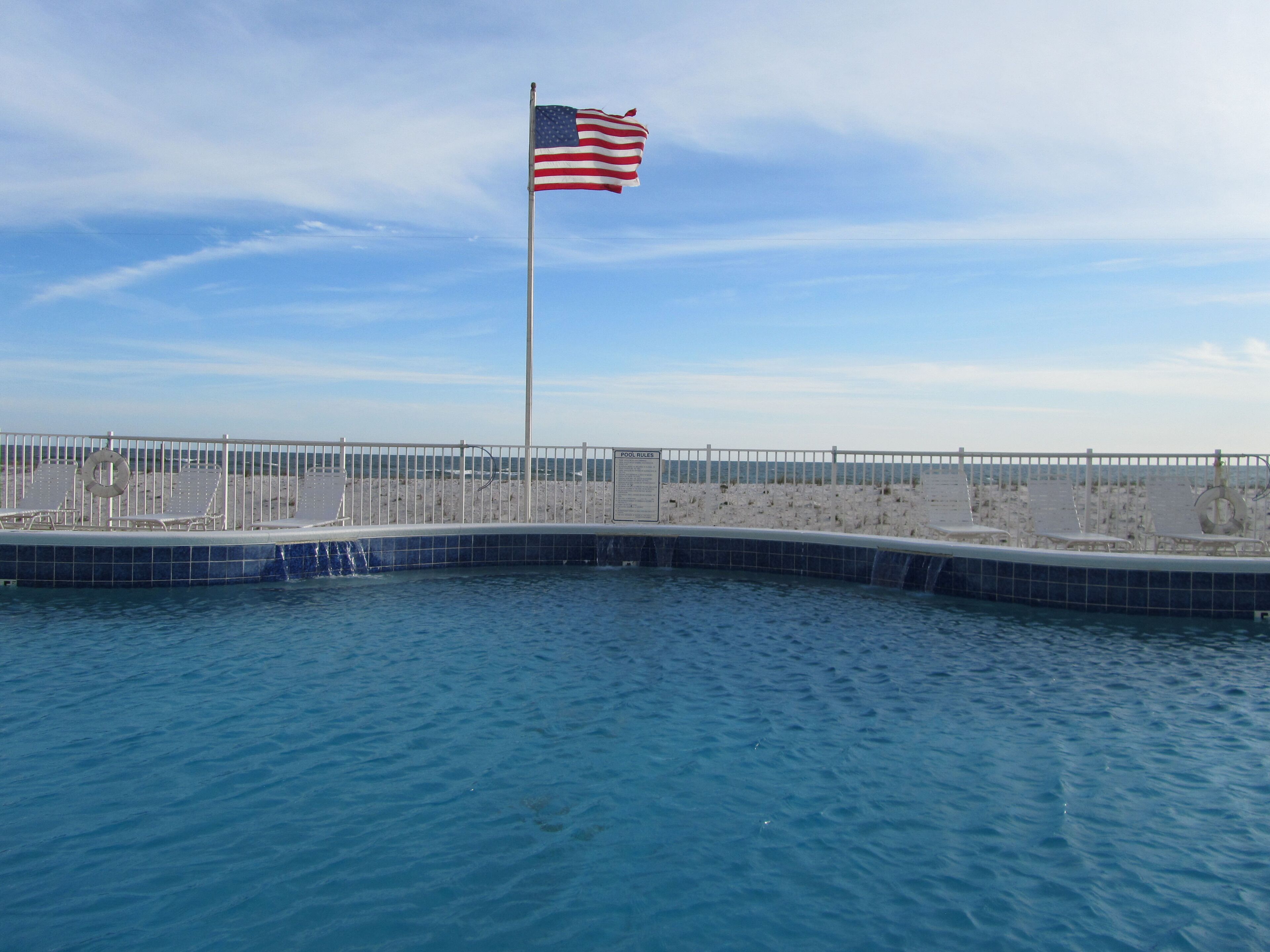 A flagpole with an American flag, a pool, and a fence.