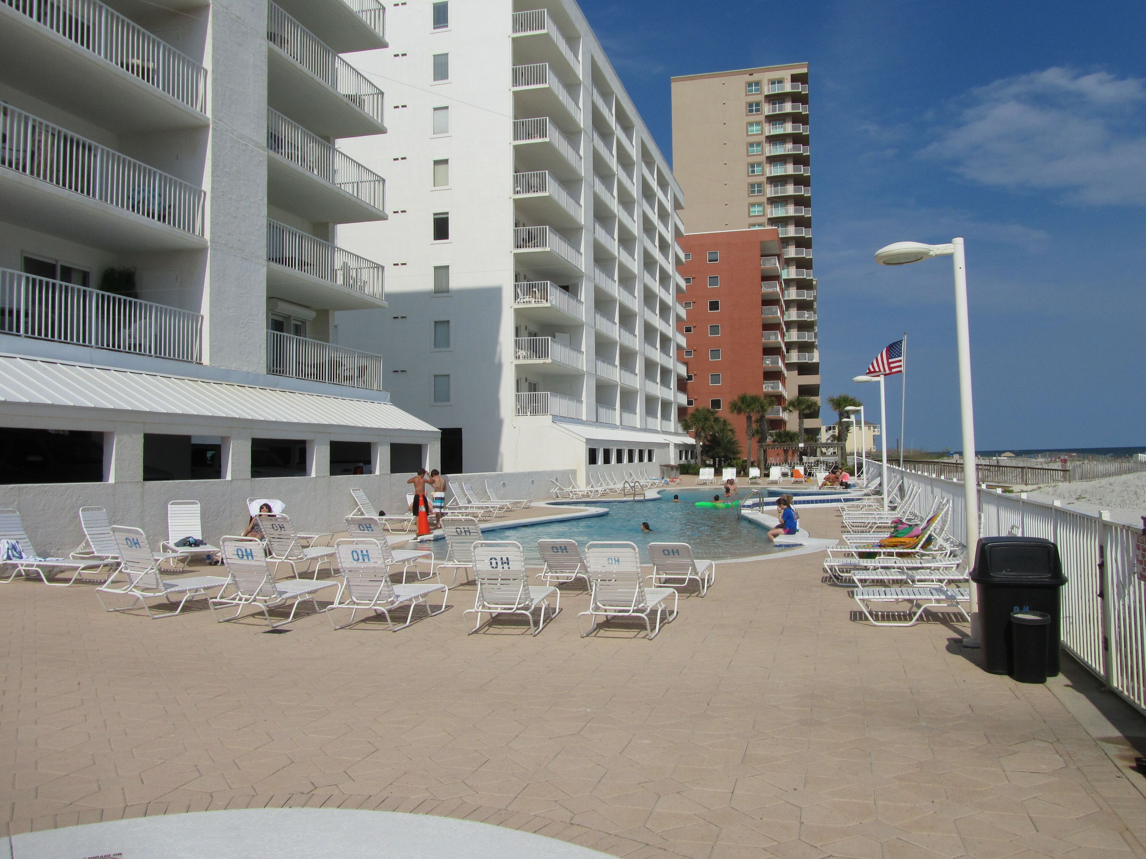 A poolside area with lounge chairs and a swimming pool, surrounded by multi-story buildings.