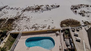 An aerial view of a beachside hotel with a swimming pool, beach chairs, and a deck area. - Clearwater Unit 7C (Gulf Shores)