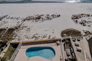 An aerial view of a beachside hotel with a swimming pool, beach chairs, and a deck area.