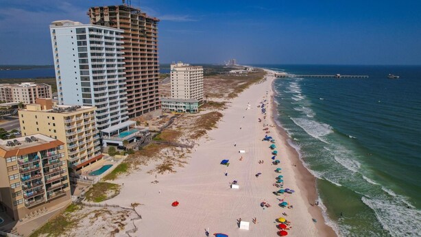 A beachfront hotel with multiple floors, a pool, and beach umbrellas. - Clearwater Unit 7C (Gulf Shores)