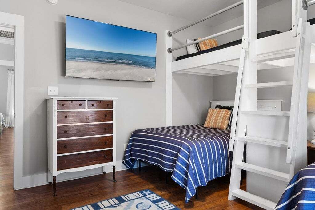 A bedroom with a bunk bed, a dresser, a painting of a beach, and a striped bedspread.