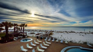 Zona de piscina con sillones de descanso, bañera de hidromasaje y vista a la playa y al océano al atardecer.