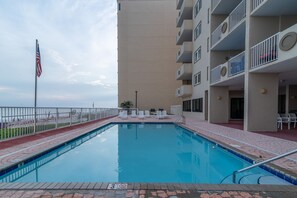 A swimming pool with a view of the beach, a flag, and a building with balconies. - Tropical Winds Unit 301 (Gulf Shores)
