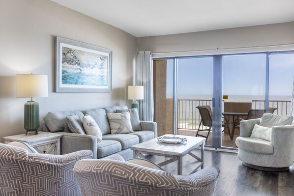 A modern living room with a grey sofa, patterned armchairs, a coffee table, and a painting on the wall. - Tropical Winds Unit 301 (Gulf Shores)