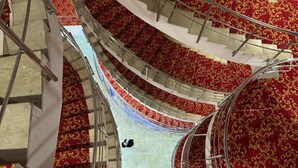 Una amplia escalera con peldaños alfombrados en rojo y barandales de metal, que conduce a varios niveles.