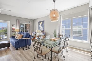 A spacious living area with a glass dining table, blue sofa, and a large window with curtains. - 214 Shoreland (Gulf Shores)