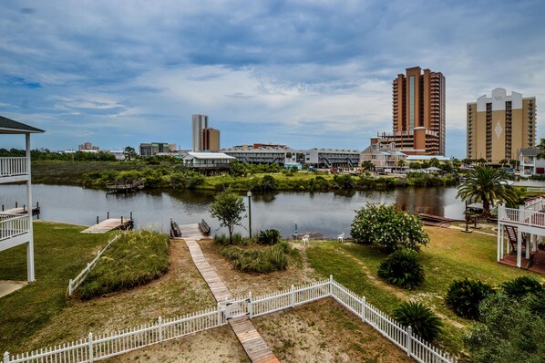 A lakeside view with a dock, grassy areas, and buildings in the background. - 214 Shoreland (Gulf Shores)