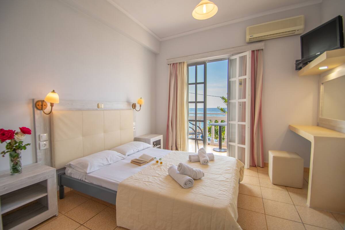 A hotel room with a bed, bedside table, lamp, air conditioning unit, and a TV.