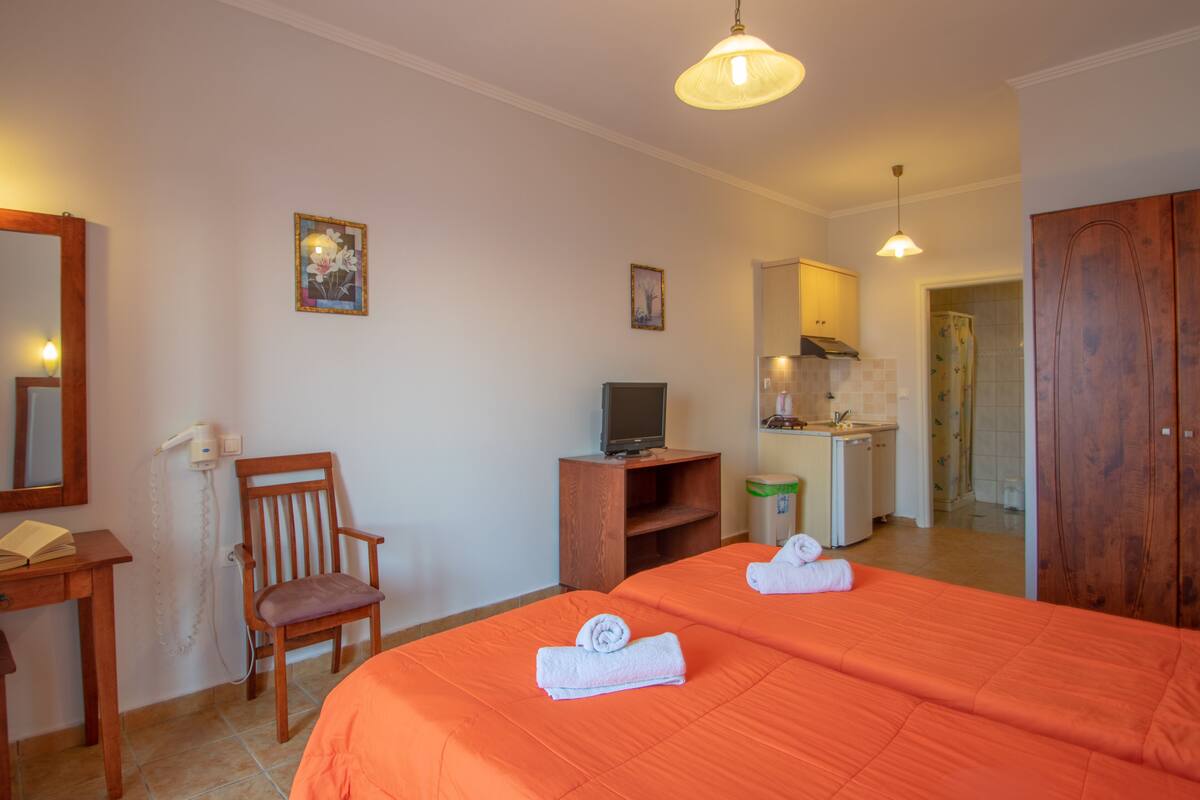 A hotel room with two beds, a desk, a chair, a television, and a small kitchenette.