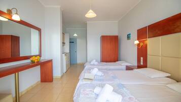 Ein Hotelzimmer mit drei Betten, einem Holztisch, einem Spiegel und einem Badezimmer im Hintergrund.