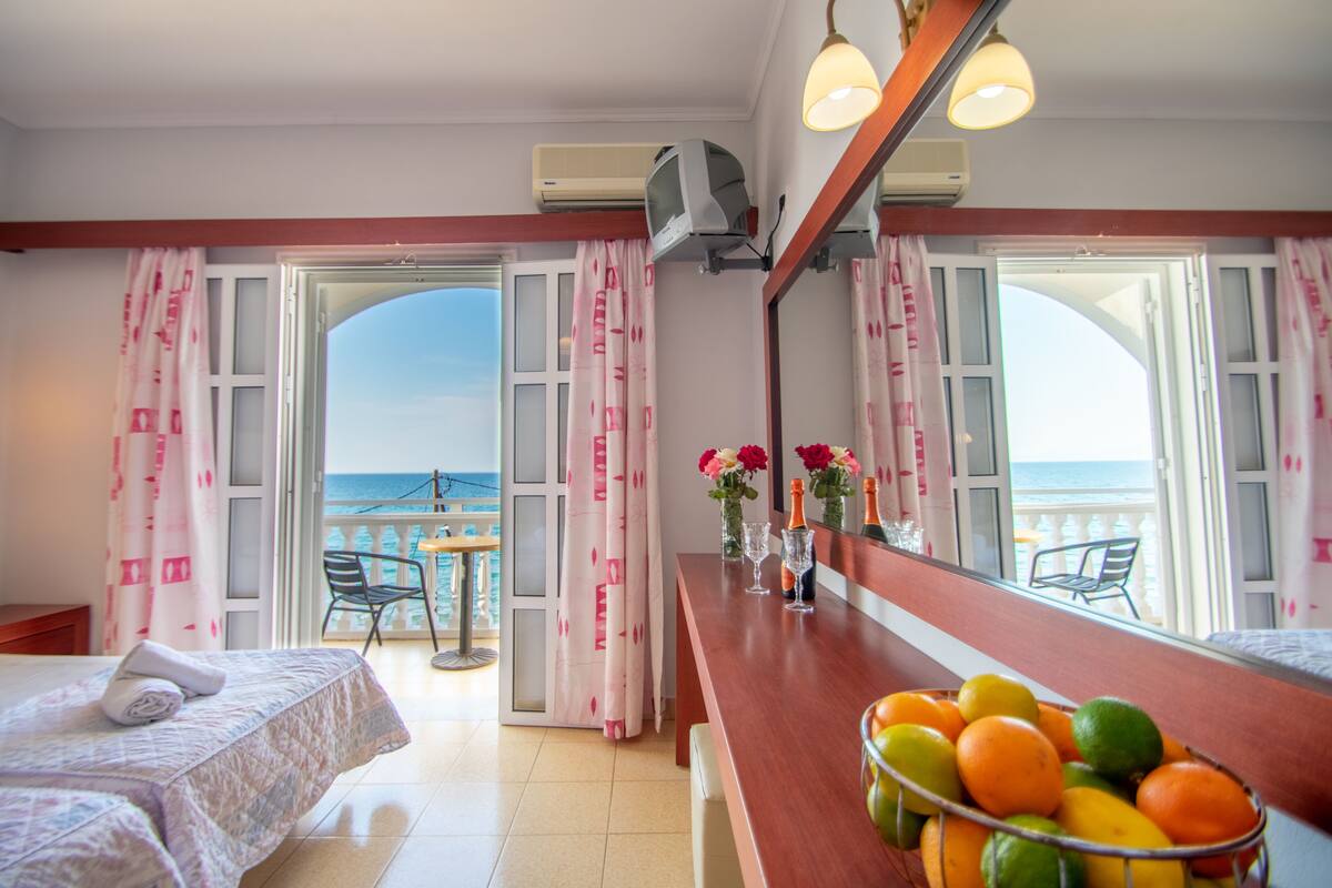 A hotel room with a balcony, a bed, a table with fruit, and a view of the sea.