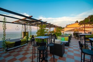 An outdoor patio with checkered flooring, seating arrangements, hanging plants, and tables.