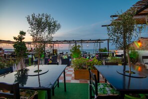 An outdoor seating area with tables and chairs, surrounded by greenery and overlooking a body of water.