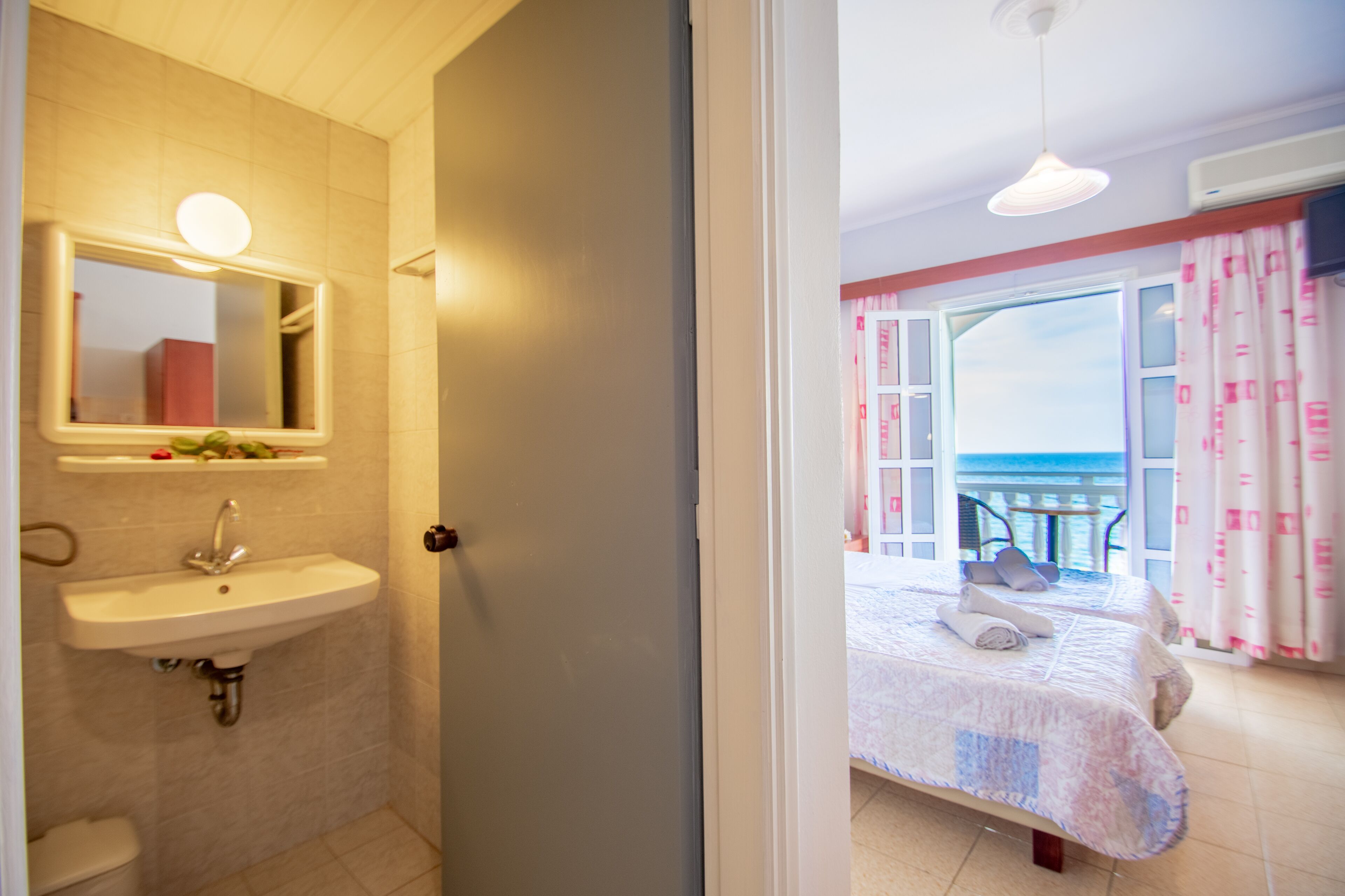 A bathroom with a sink and mirror, a door leading to a balcony with a view.