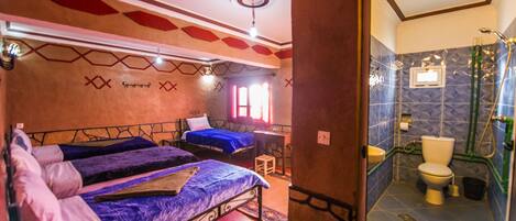 A room with two beds, a small table, and a bathroom with a shower and toilet.