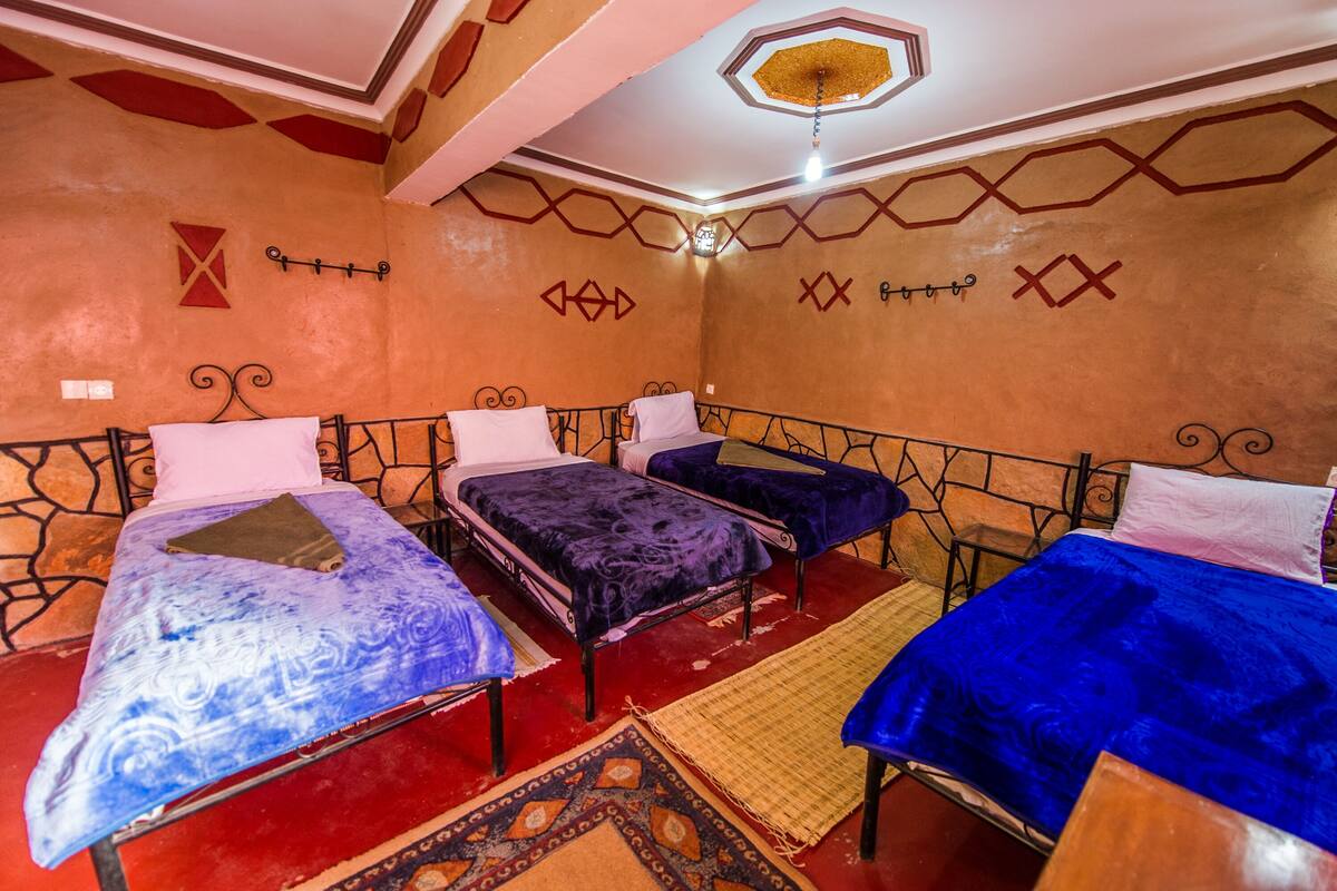 A room with three beds, each with a different colored bedspread. The walls have geometric patterns and a red and white color scheme.