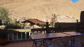 A terrace with a table and chairs, overlooking a mountainous landscape and a village. -  Les Jardins de Todgha (Toudgha El Oulia)