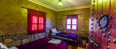 A room with two beds, a stone wall, a wooden cabinet, and a window with red curtains.