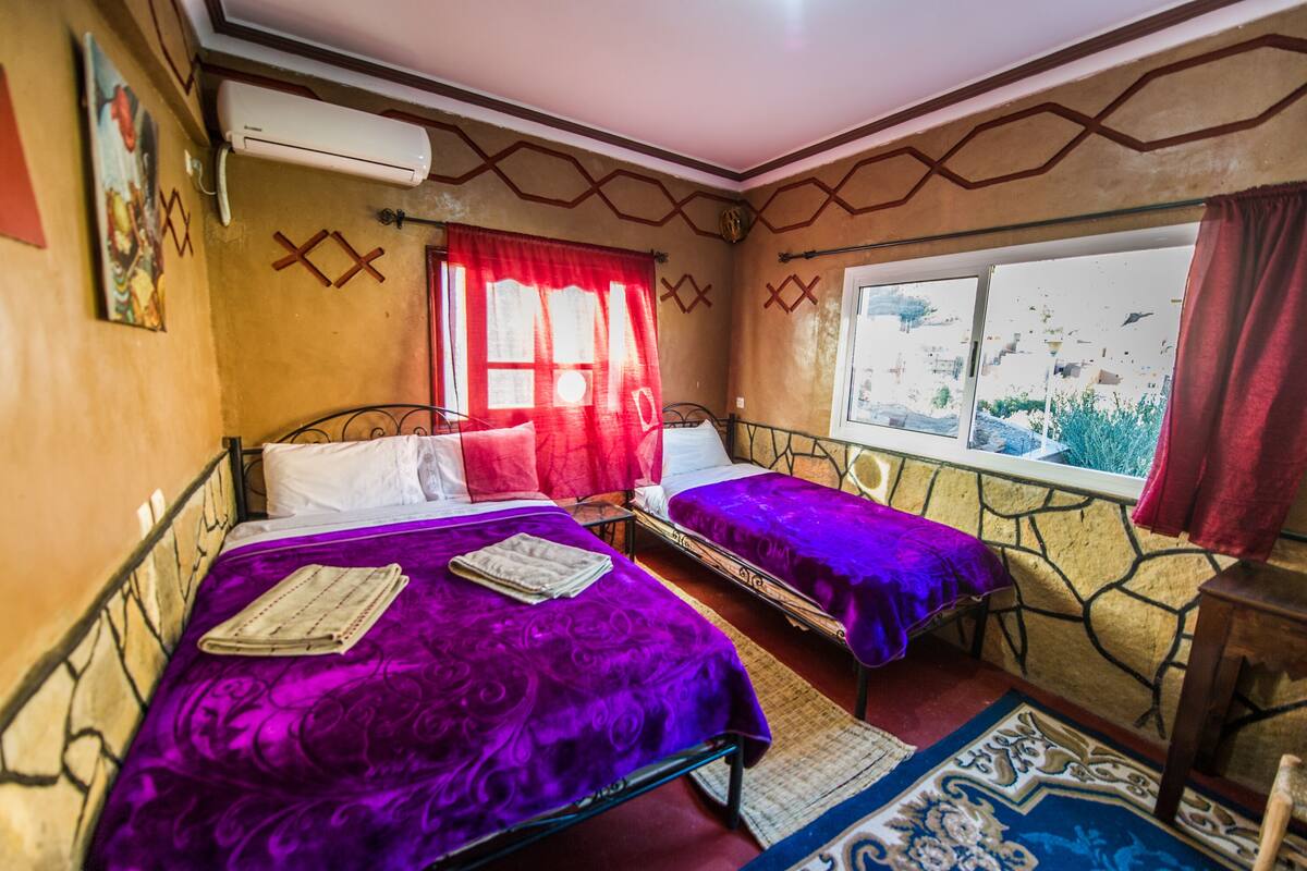 A room with two beds, a window with a view, and a patterned rug.