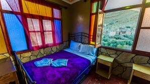 A room with a bed, a window with a view of a town, and a stone wall. -  Les Jardins de Todgha (Toudgha El Oulia)