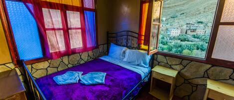 Una habitación con una cama, un ventanal con vistas a un pueblo y una pared de piedra.