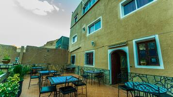 An outdoor patio with tables and chairs, a building with multiple windows, and a tiled floor.