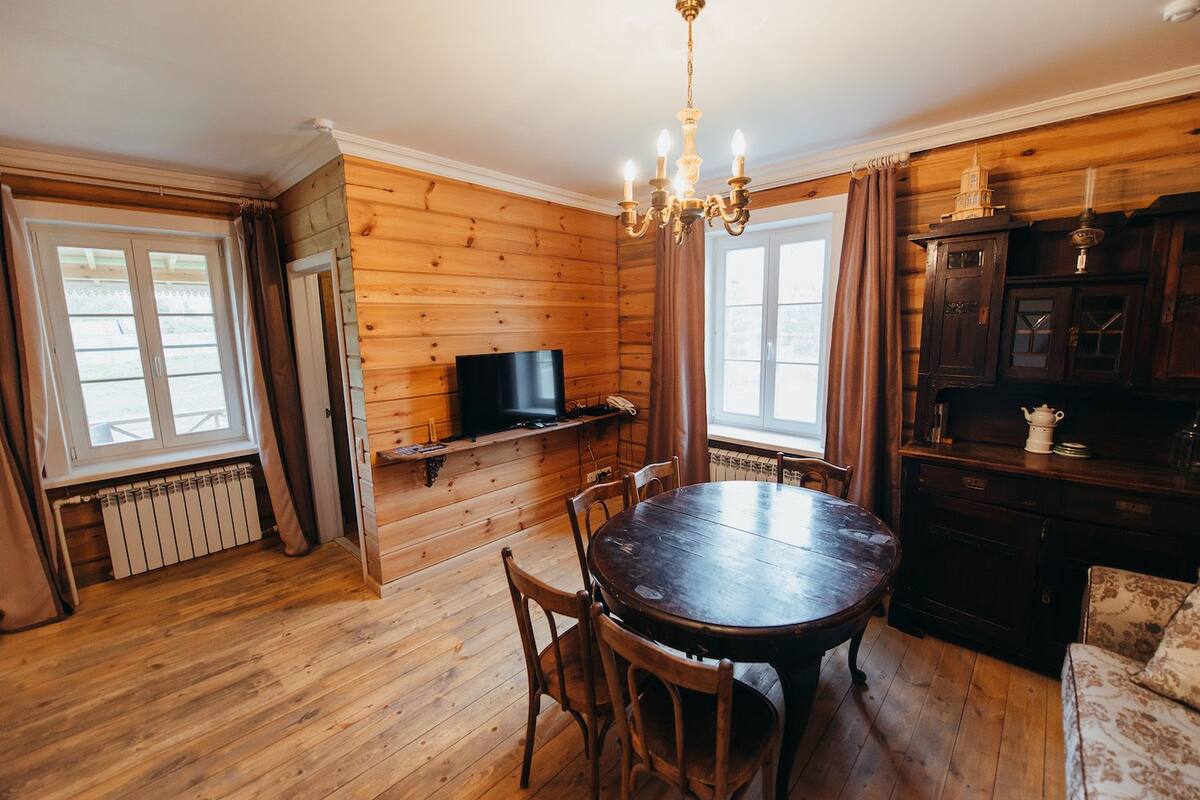 Ein Holzinterieur mit einem runden Esstisch, Stühlen, einem Fernseher auf einem Regal und einer Deckenleuchte.