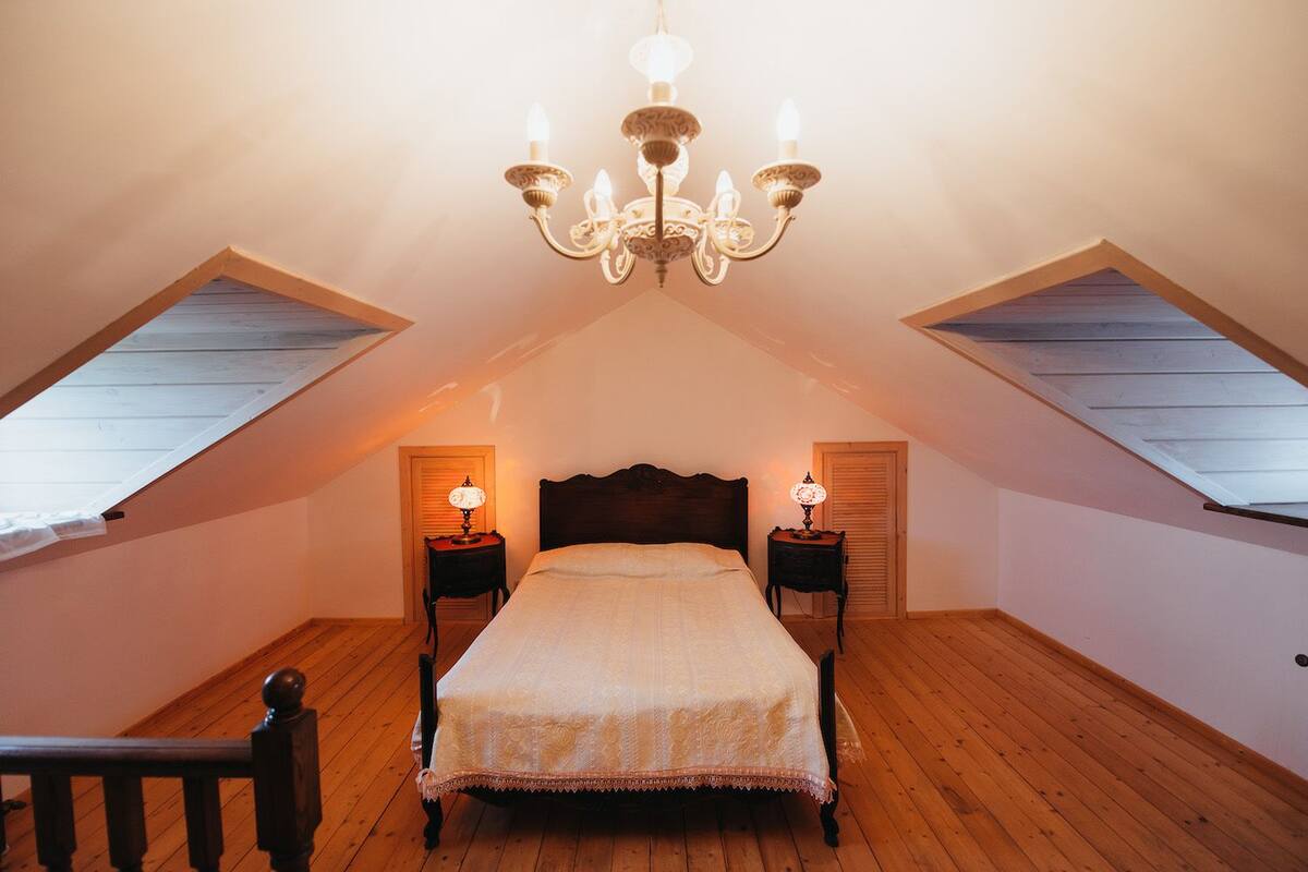 Ein Schlafzimmer mit schrägverdeckter Decke, einem Bett, zwei Nachttischen mit Lampen und einer Deckenleuchte.