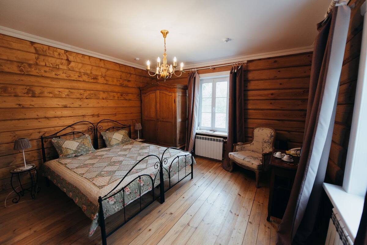 Ein Schlafzimmer mit Holzwänden, einem Bett, einem Stuhl, einem Tisch und einem Fenster.