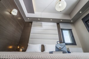 A modern bedroom with a sloped ceiling, recessed lighting, a window, and a bed with pillows and a handbag.
