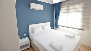 A bedroom with a bed, white bedding, a bedside table, an air conditioning unit, a window with curtains, and a ceiling light. - Artim Exclusive Apart Hotel (Fethiye)