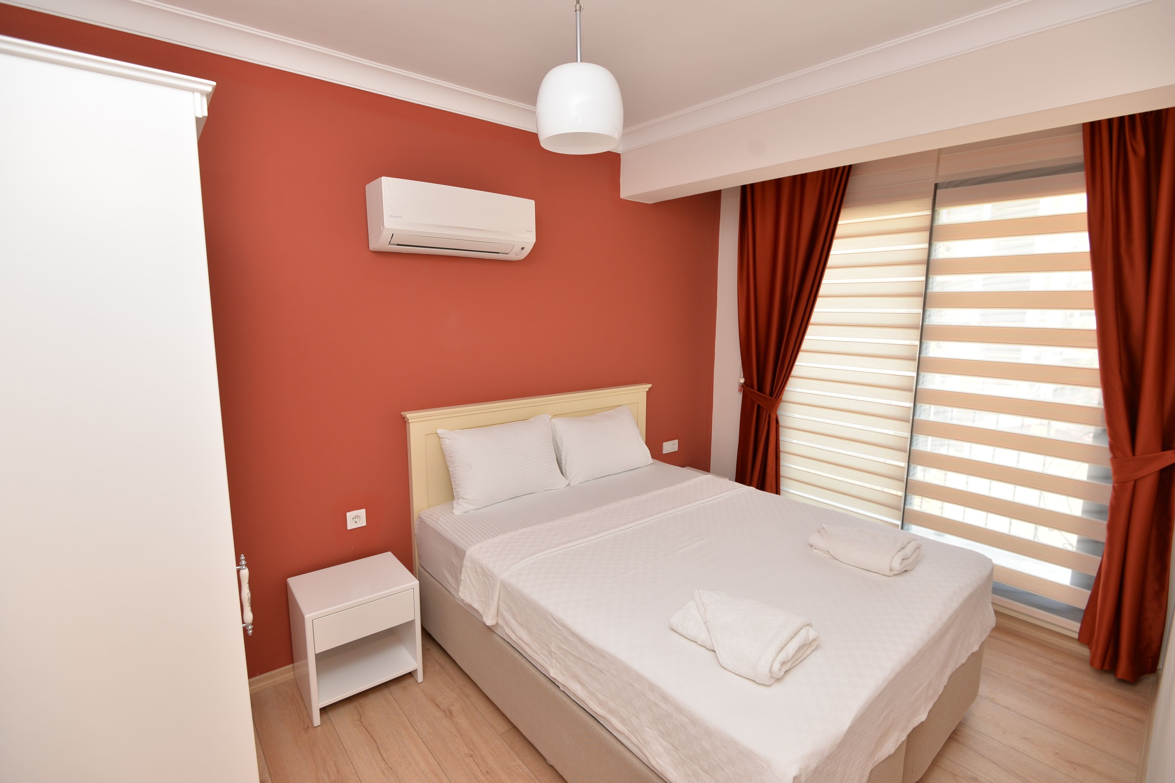 A bedroom with a bed, white nightstand, and an air conditioning unit on the wall.