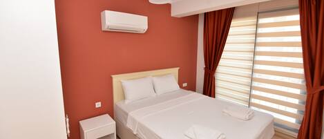 A bedroom with a bed, white nightstand, and an air conditioning unit on the wall.