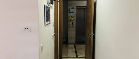 A narrow hallway with a wooden door at the end, a wall socket, and a poster.