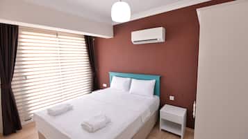 A neatly made bed with white linens and towels, a white bedside table, and a white air conditioning unit on a wall.