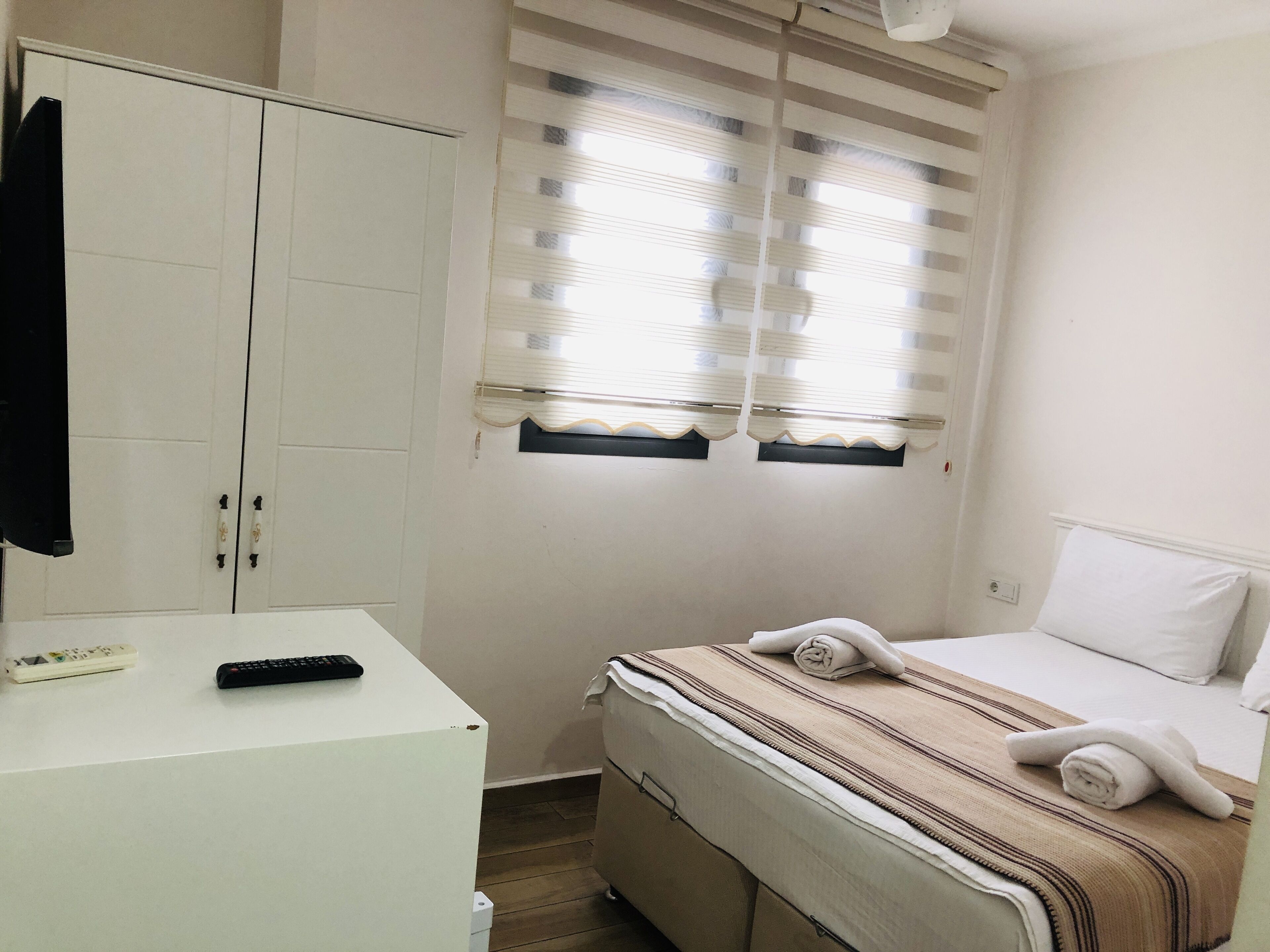 A bedroom with a bed, a bedside table, a wardrobe, and a window with blinds.